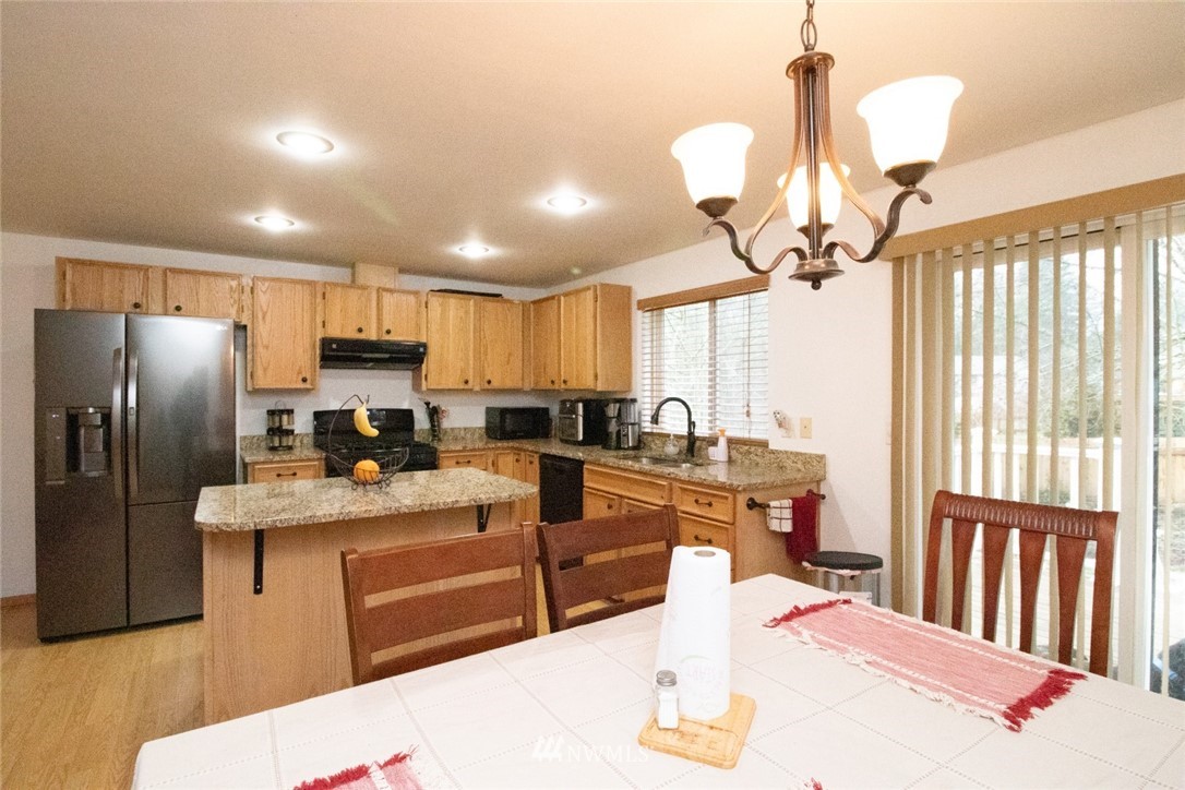 214 Fern Meadows Loop Southeast Port Orchard, WA 98366 - Photo 7 of 23 a kitchen with stainless steel appliances kitchen island granite countertop a refrigerator a sink dishwasher a dining table and chairs with wooden floor