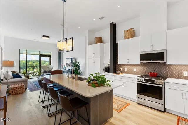 a kitchen with stainless steel appliances a stove a sink a microwave a dining table and chairs with wooden floor