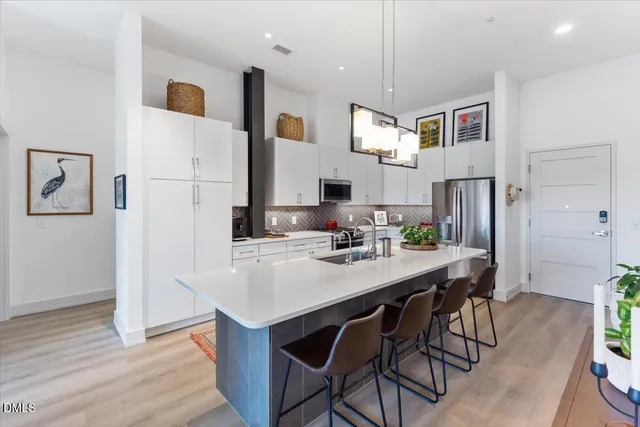 a kitchen with stainless steel appliances kitchen island granite countertop a refrigerator a sink dishwasher a stove with white cabinets and wooden floor