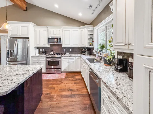 a large kitchen with stainless steel appliances granite countertop a stove top oven a sink dishwasher and wooden cabinets with wooden floor