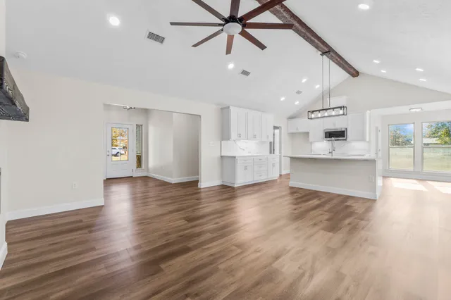 a view of an empty room and kitchen with ceiling fan wooden floor and windows