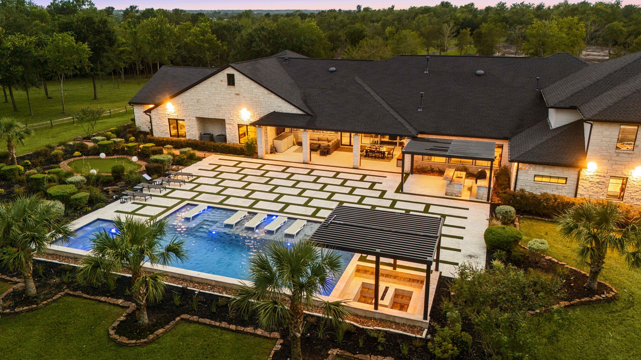 1100 Felder Road Washington, TX 77880 - Photo 1 of 50 A resort-style backyard anchors the estate, a gunite pool with tanning ledge, a sunken fire-pit lounge, an outdoor kitchen, and a putting green, all set against the home's stone elevation.