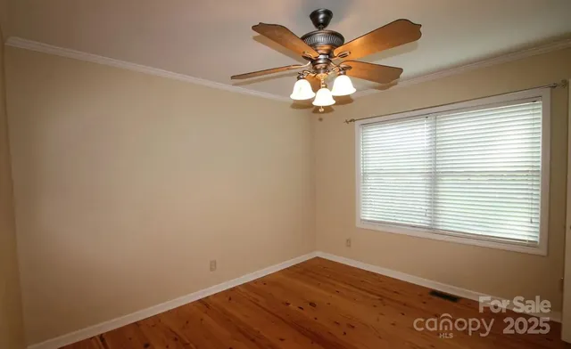 an empty room with wooden floor chandelier fan and windows