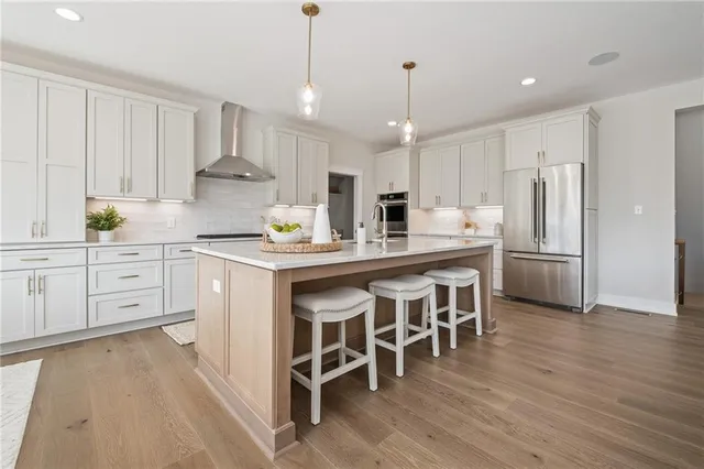 a kitchen with stainless steel appliances kitchen island granite countertop a refrigerator a stove a sink and white cabinets with wooden floors