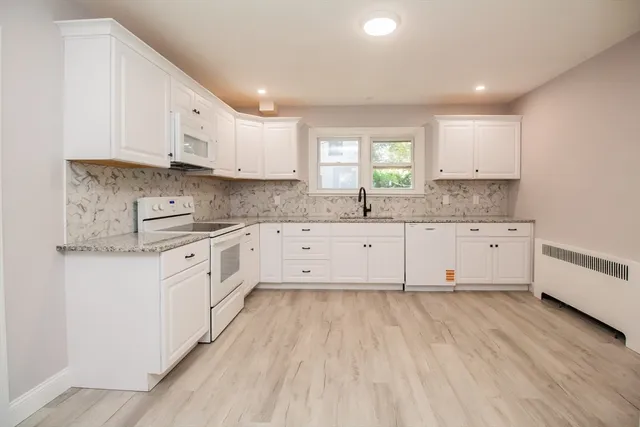 a large white kitchen with granite countertop a stove a sink a refrigerator and white cabinets with wooden floor