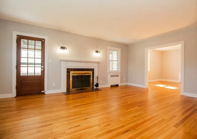 an empty room with wooden floor fireplace and windows