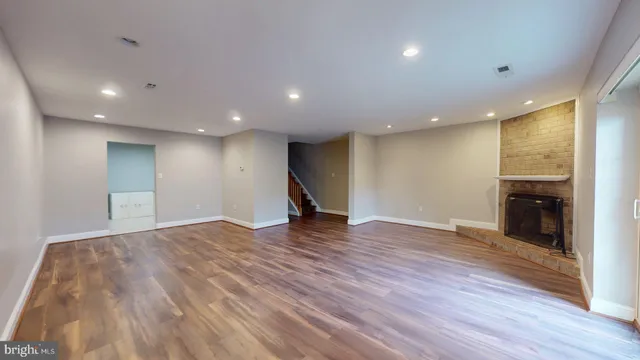 a view of an empty room with wooden floor kitchen and a window