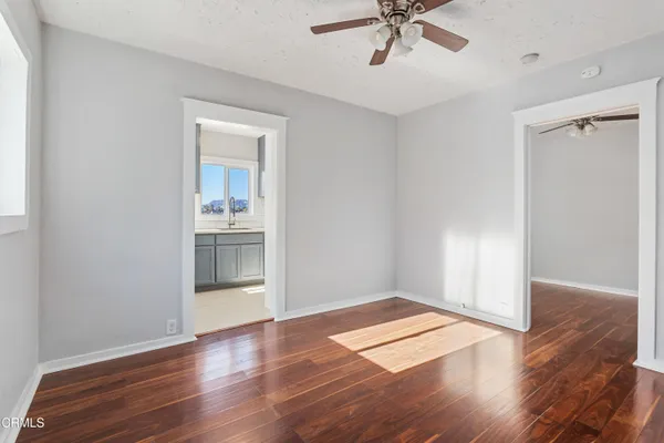 an empty room with wooden floor a ceiling fan and kitchen view