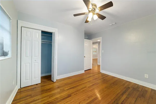 an empty room with wooden floor closet and fan