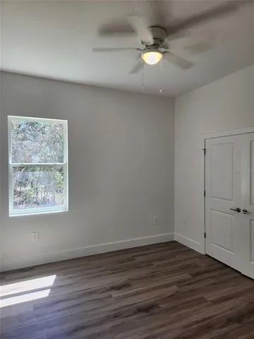 an empty room with wooden floor chandelier fan and windows