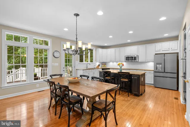 a kitchen with stainless steel appliances granite countertop a stove a refrigerator a sink a dining table and chairs with wooden floor