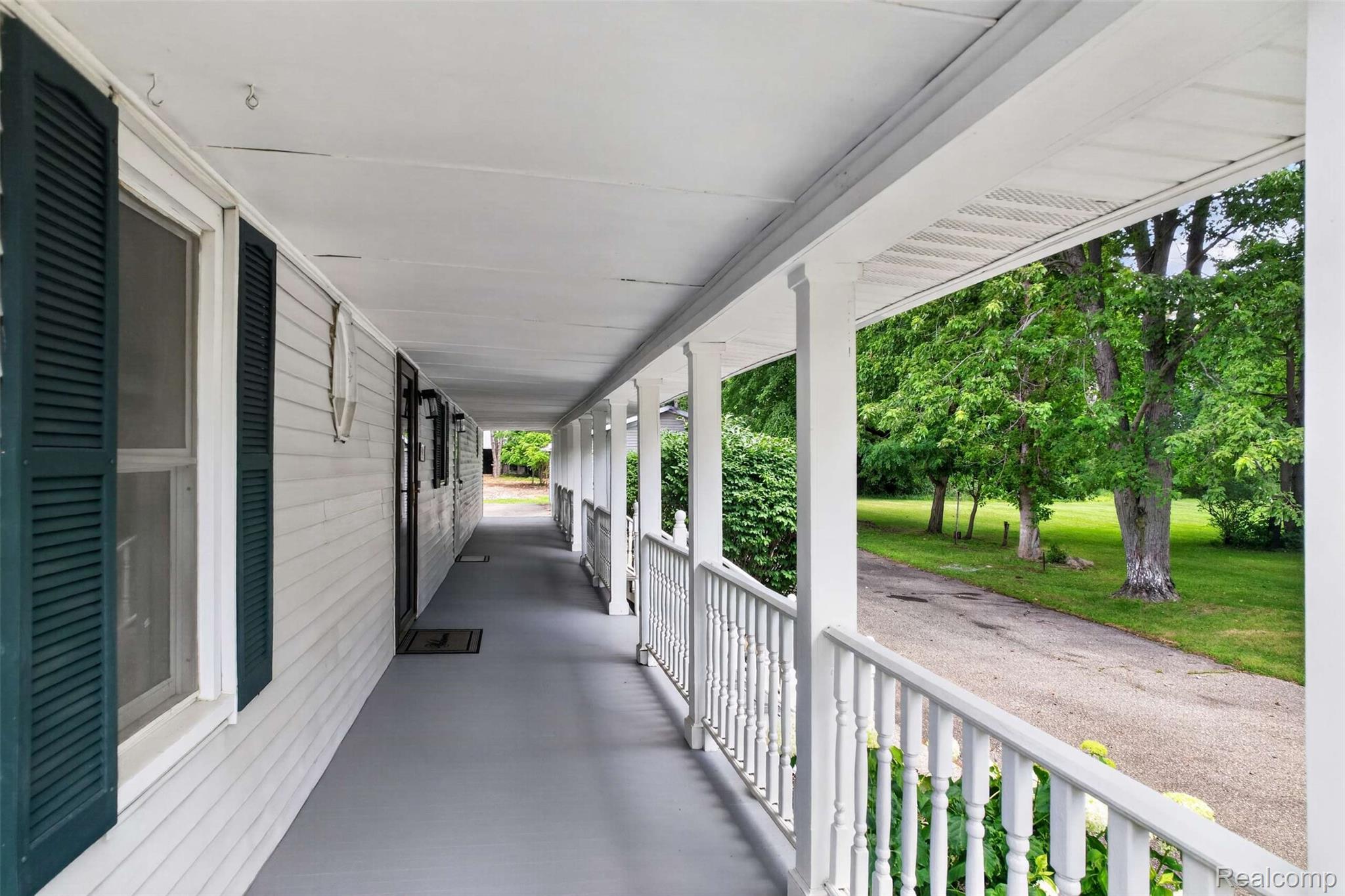 Expansive covered porch featuring a painted gray floor, white railing, and multiple support columns