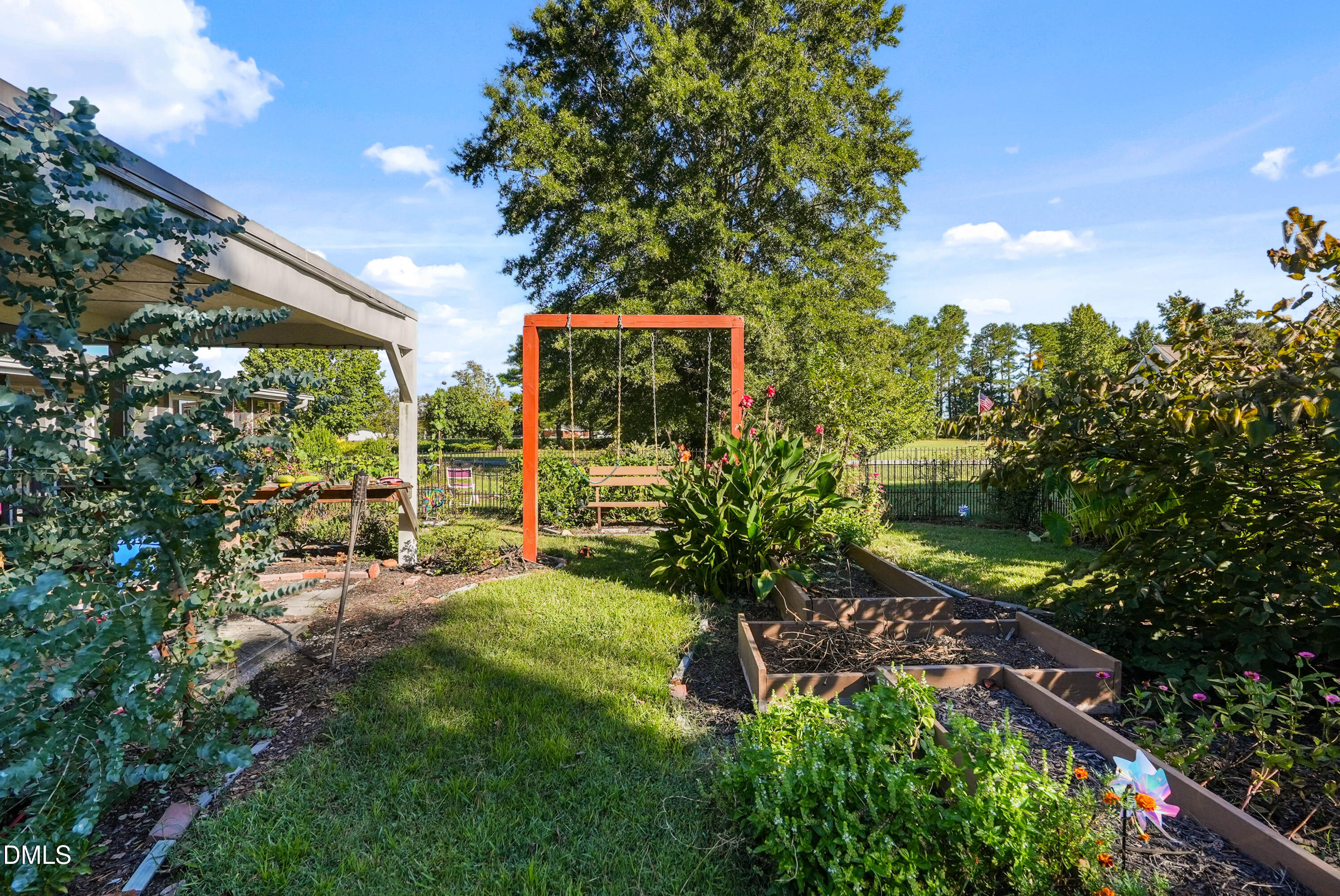 7406 Old Beulah Road Kenly, NC 27542 - Photo 23 of 30 Covered patio with a landscaped yard, featuring a swing set, raised garden beds, and mature plantings