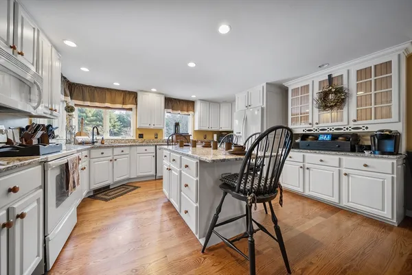 a kitchen with stainless steel appliances granite countertop wooden cabinets a sink a stove a refrigerator and island with wooden floor