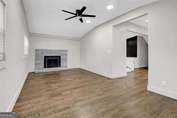 an empty room with wooden floor a ceiling fan a fireplace and entryway