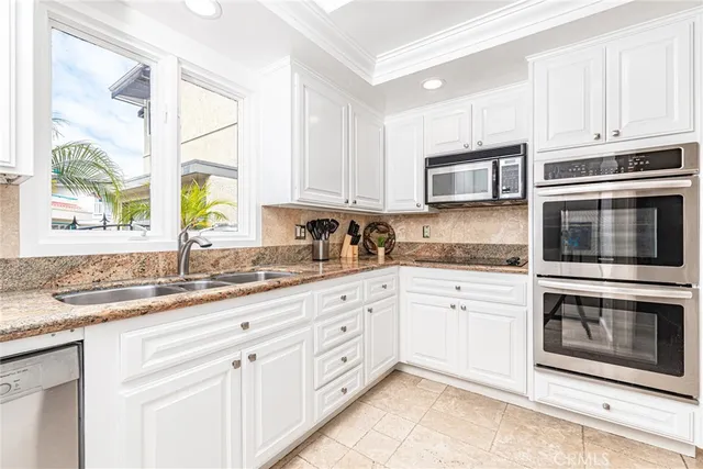 a kitchen with granite countertop white cabinets stainless steel appliances a sink and a window
