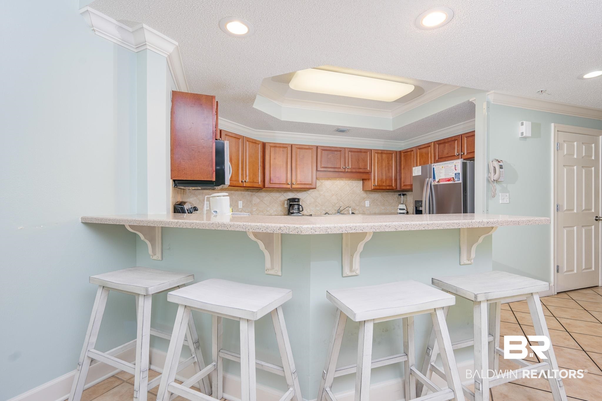 27580 Canal Road, Unit 1322 Orange Beach, AL 36561 - Photo 8 of 30 Kitchen featuring crown molding, light countertops, brown cabinets, backsplash, and stainless steel refrigerator with ice dispenser