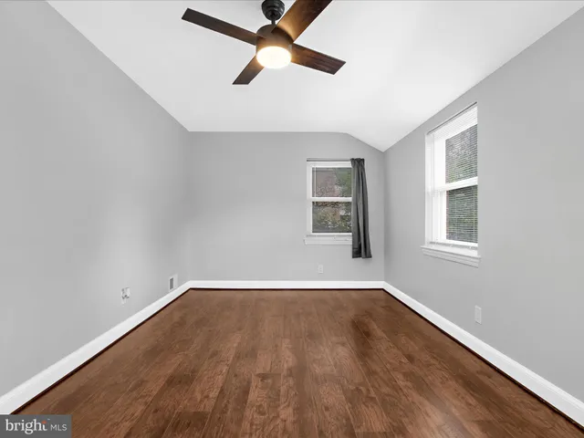 an empty room with wooden floor ceiling fan and windows