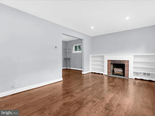 a view of an empty room with wooden floor fireplace and a window