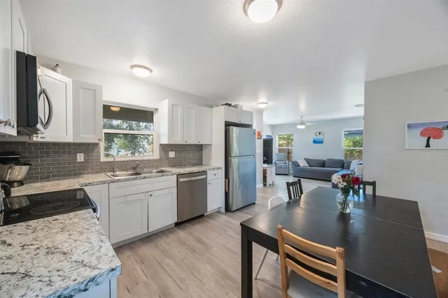 a kitchen with stainless steel appliances granite countertop a refrigerator a stove a sink a dining table and chairs with wooden floor