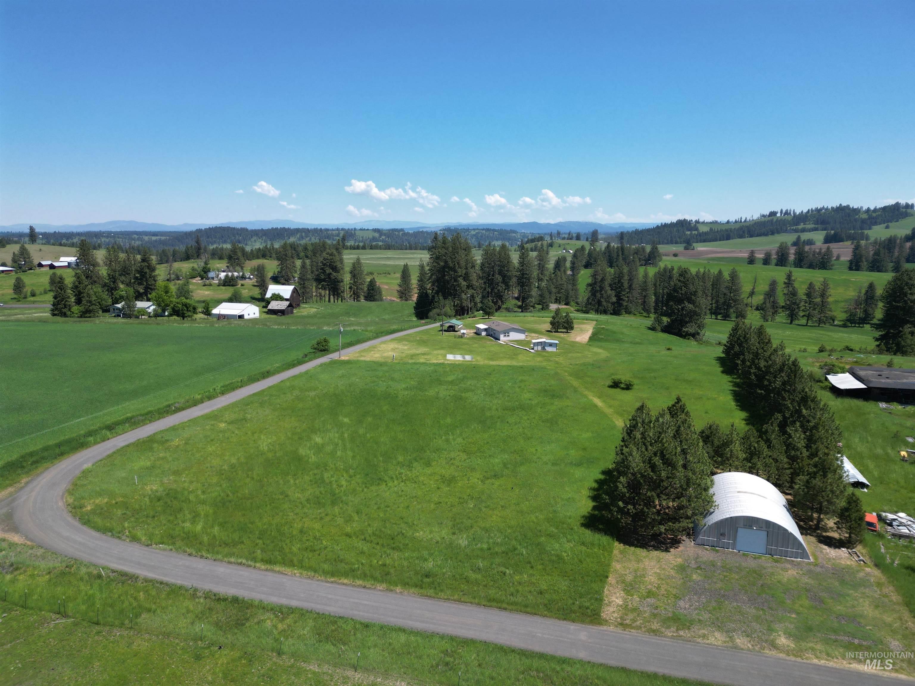 135 Harrisburg Road Kamiah, ID 83536 - Photo 16 of 41 Expansive rural property featuring a winding driveway, multiple outbuildings, agricultural fields, and distant tree-lined hills