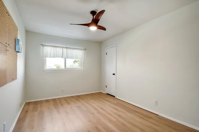 an empty room with wooden floor ceiling fan and windows