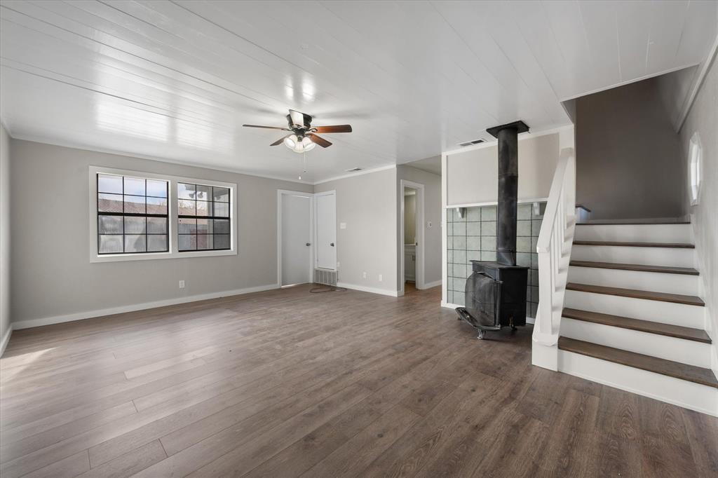 443 County Road 3799 Springtown, TX 76082 - Photo 16 of 33 Unfurnished living room featuring a wood stove, dark wood-type flooring, stairway, crown molding, and ceiling fan