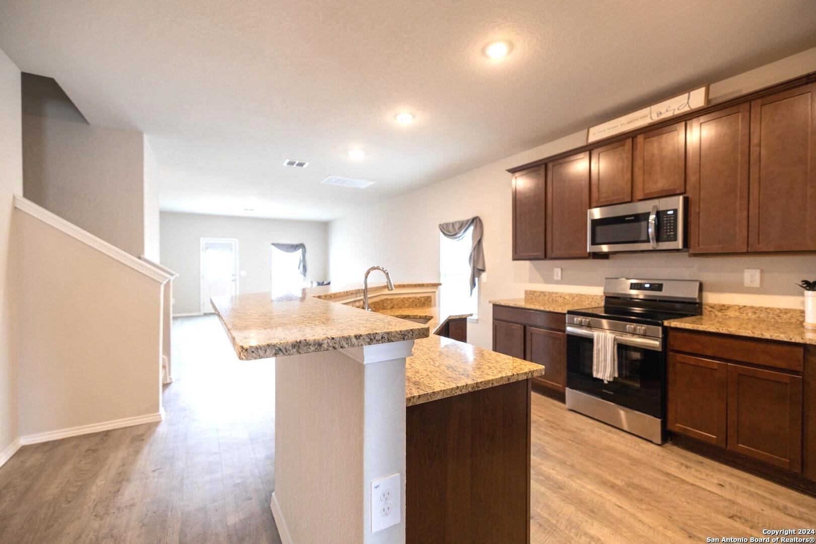 3431 Andromeda Way Converse, TX 78109 - Photo 6 of 24 a kitchen with kitchen island granite countertop wooden floors and stainless steel appliances