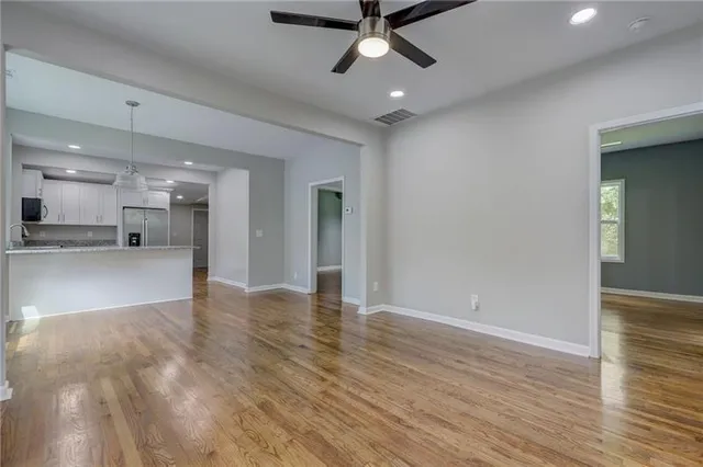 a view of an empty room and kitchen view with wooden floor