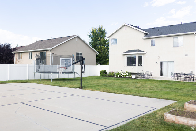 1204 North 3020th Street West Provo, UT 84601 - Photo 8 of 35 Expansive concrete sport court with defined lines in a spacious backyard featuring a manicured lawn, white vinyl fencing, a ground-level patio, and built-in planting boxes