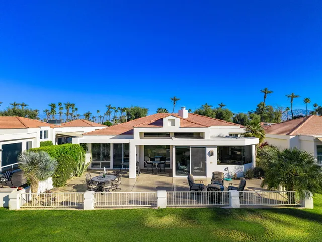 a patio with couches table and chairs with swimming pool in front of house