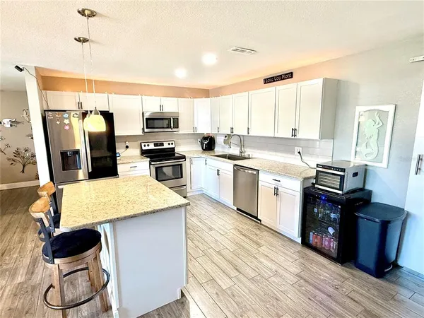 a kitchen with stainless steel appliances granite countertop a stove top oven a sink a refrigerator white cabinets and wooden floor