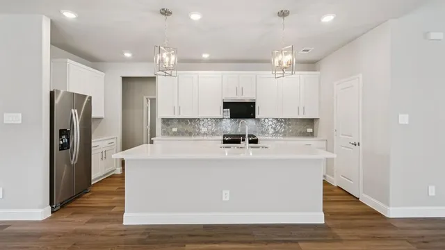 a large kitchen with kitchen island a stove a refrigerator a sink and white cabinets with wooden floor