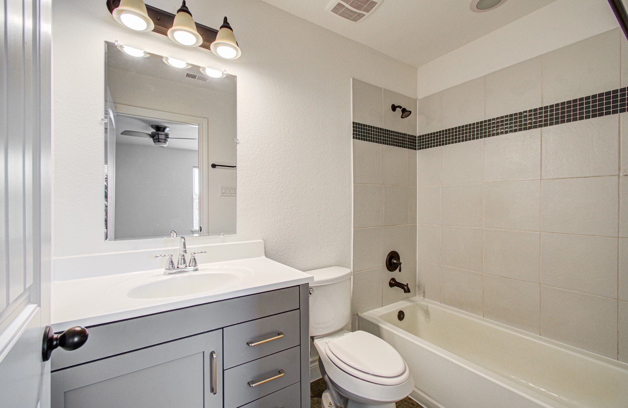 6621 North Main Street Houston, TX 77009 - Photo 29 of 41 Bright and modern bathroom with a sleek vanity, large mirror, and overhead lighting. Features a tiled bathtub and shower combination with dark fixtures and accent tiles.