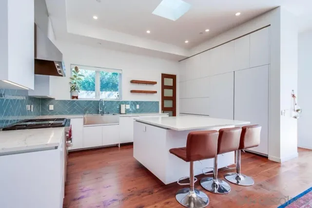 a kitchen with stainless steel appliances granite countertop a stove top oven a sink dishwasher a dining table and chairs with wooden floor