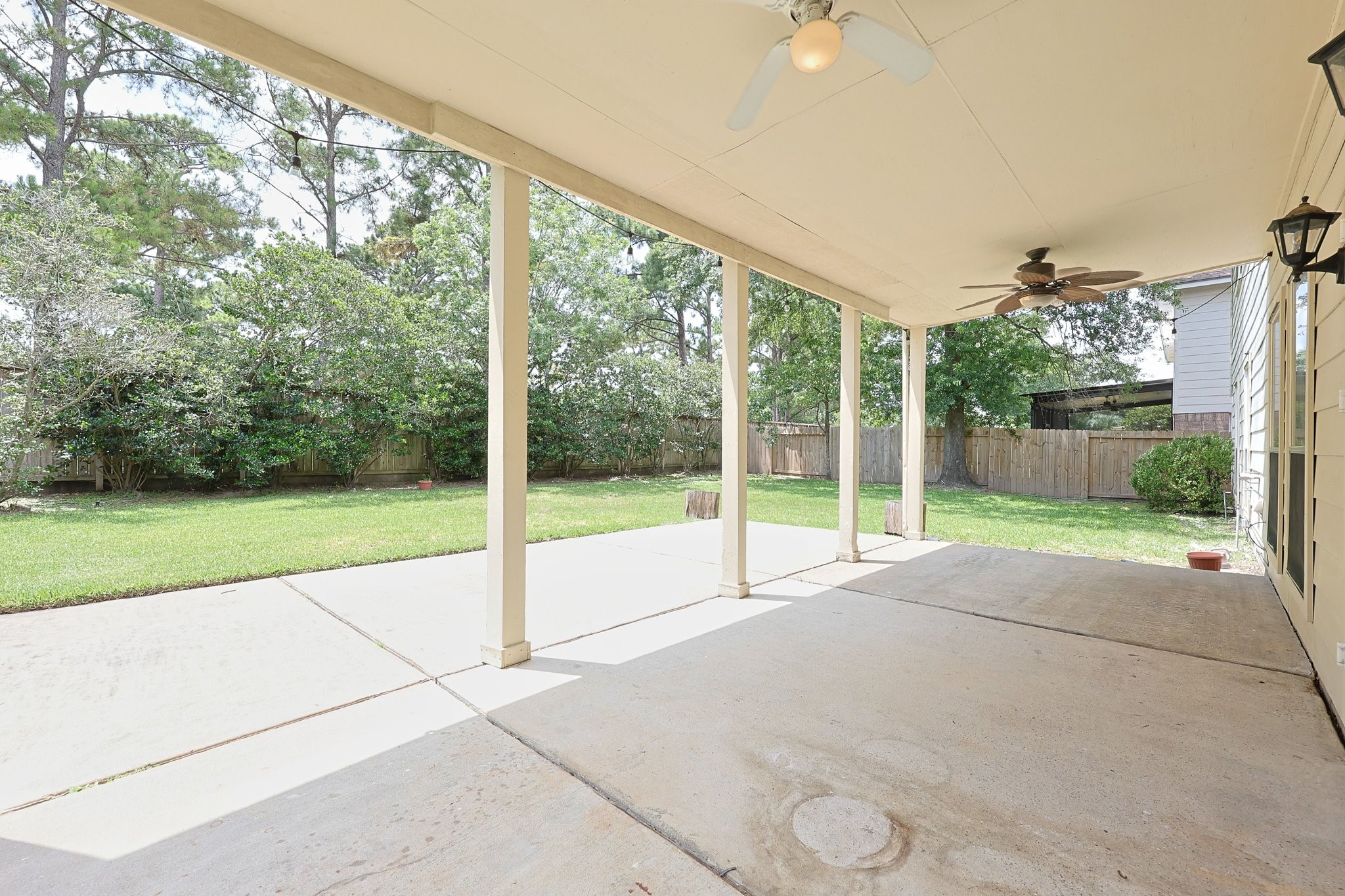 23019 Eastgate Village Drive Spring, TX 77373 - Photo 41 of 46 Spacious covered patio with ceiling fans, overlooking a well-maintained, fenced backyard surrounded by mature trees, perfect for outdoor relaxation and entertaining.