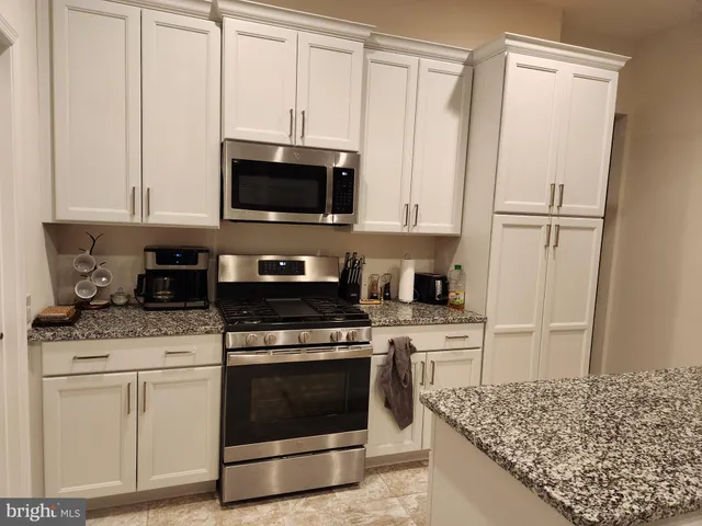 a kitchen with stainless steel appliances granite countertop a stove a refrigerator and a white cabinets