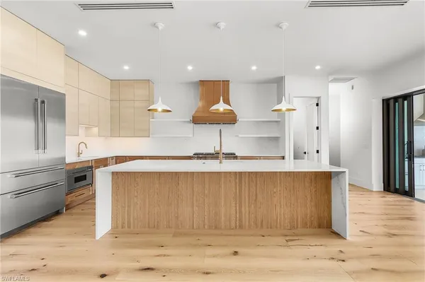 a kitchen with stainless steel appliances granite countertop a sink a stove a refrigerator and a dining table with wooden floor