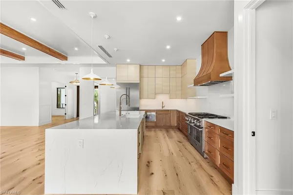 a large kitchen with stainless steel appliances a large counter top a stove a chimney a sink and a refrigerator