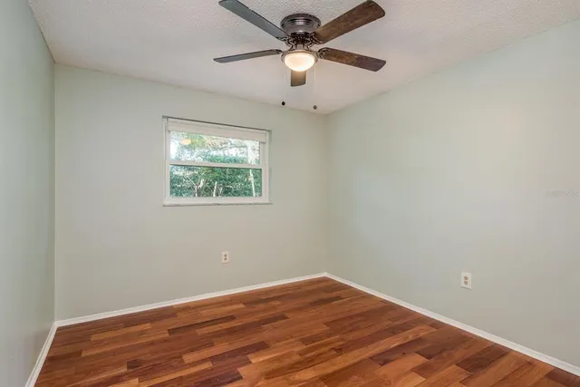 an empty room with wooden floor ceiling fan and windows