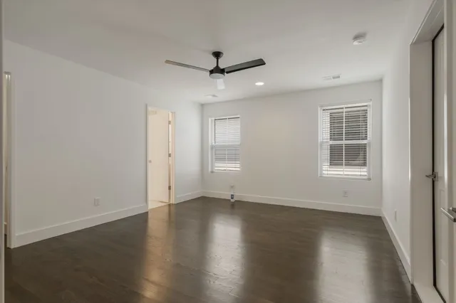 an empty room with wooden floor ceiling fan and windows