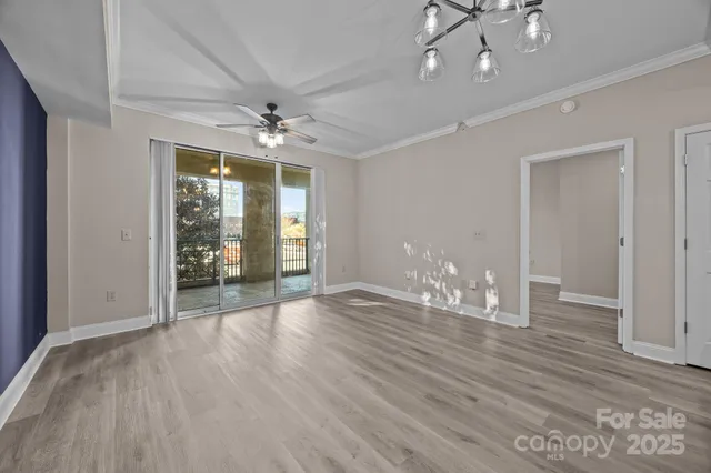 a view of an empty room with wooden floor and a ceiling fan