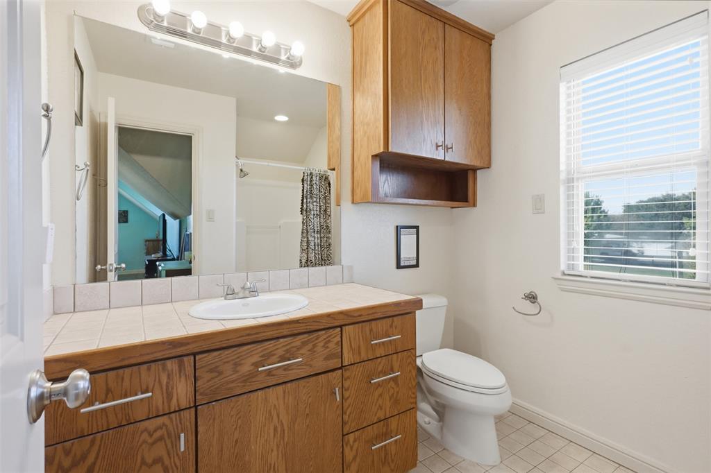 207 Dennis Road Lipan, TX 76462 - Photo 28 of 40 Bathroom featuring a single vanity with wood-finish cabinetry, a tiled countertop, and an integrated sink