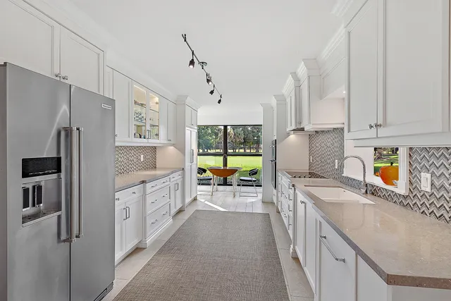 a kitchen with stainless steel appliances granite countertop a refrigerator a sink dishwasher a oven and white cabinets with wooden floor