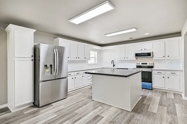 a kitchen with stainless steel appliances granite countertop a refrigerator a stove top oven a sink and dishwasher with wooden floor