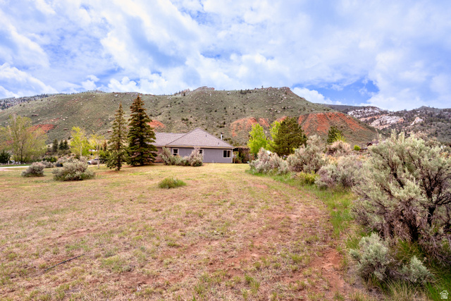 7343 North Sawtooth Cv Road Vernal, UT 84078 - Photo 62 of 64 Expansive property featuring a grey exterior residence with a brown roof, mature evergreen trees, scattered shrubs, and a prominent mountainous backdrop