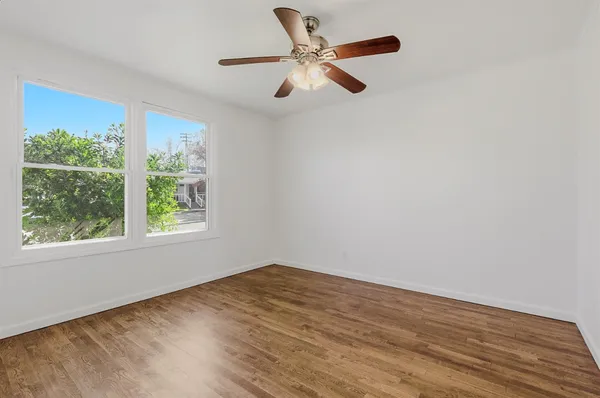 an empty room with wooden floor fan and windows