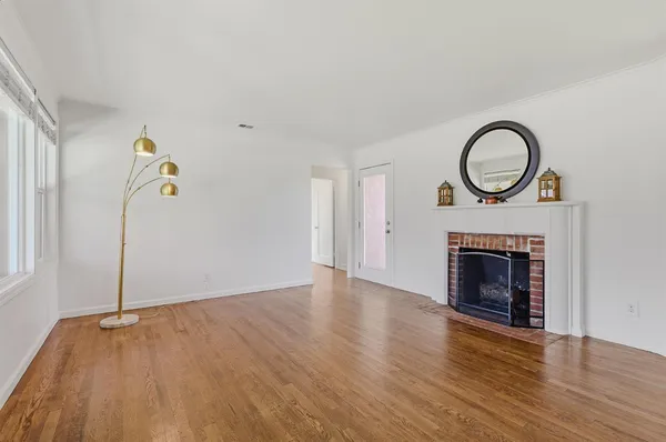 a view of an empty room with wooden floor fireplace and a window
