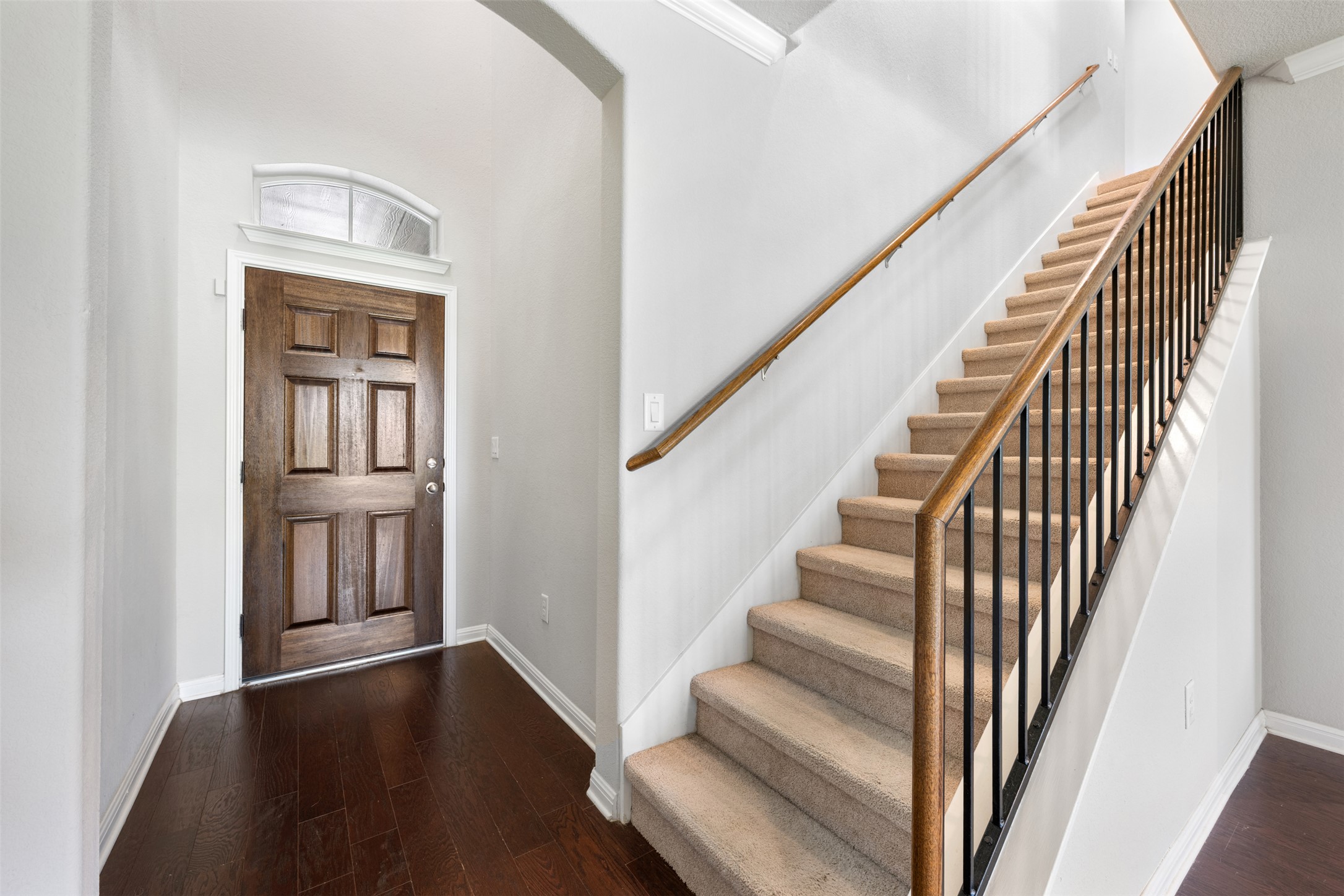 211 Parable Cove Pflugerville, TX 78660 - Photo 20 of 40 Entryway featuring rich wood-finish flooring, a paneled wood-finish door with an arched transom window, and a carpeted staircase with wood handrails and black metal balusters