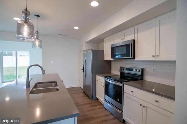 a kitchen with stainless steel appliances a stove a sink a microwave a refrigerator white cabinets and a wooden floor